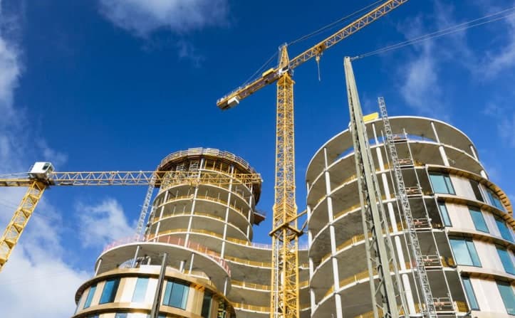 Two curved towers under construction beside tall cranes